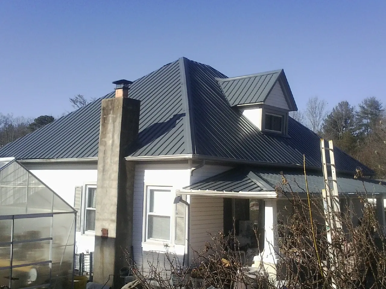Dark blue standing seam metal roof on a white farmhouse with dormer — Slate & Tile Roof Repair by Roofing Brothers in Mulberry