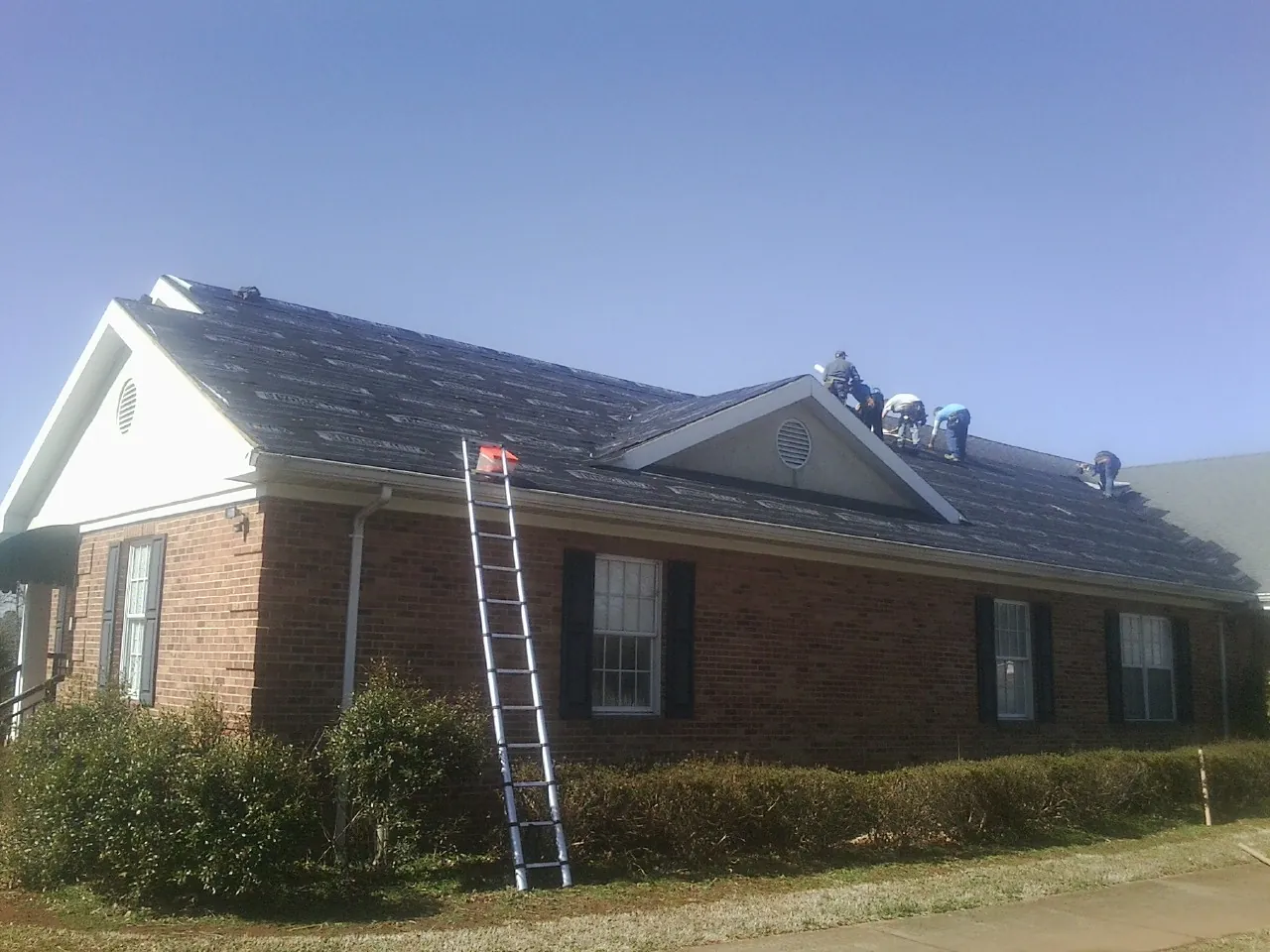 Crew tearing shingles off a brick ranch roof with a ladder set — Emergency Roof Repair work by our crew in Mulberry