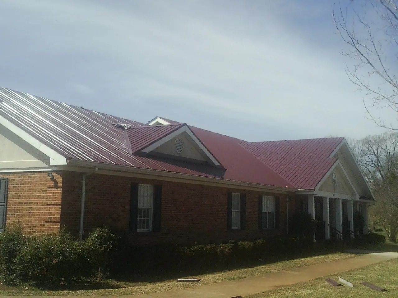 Red metal roof with gabled entries on a long brick building, from a Hail Damage Roof Repair job in Mulberry