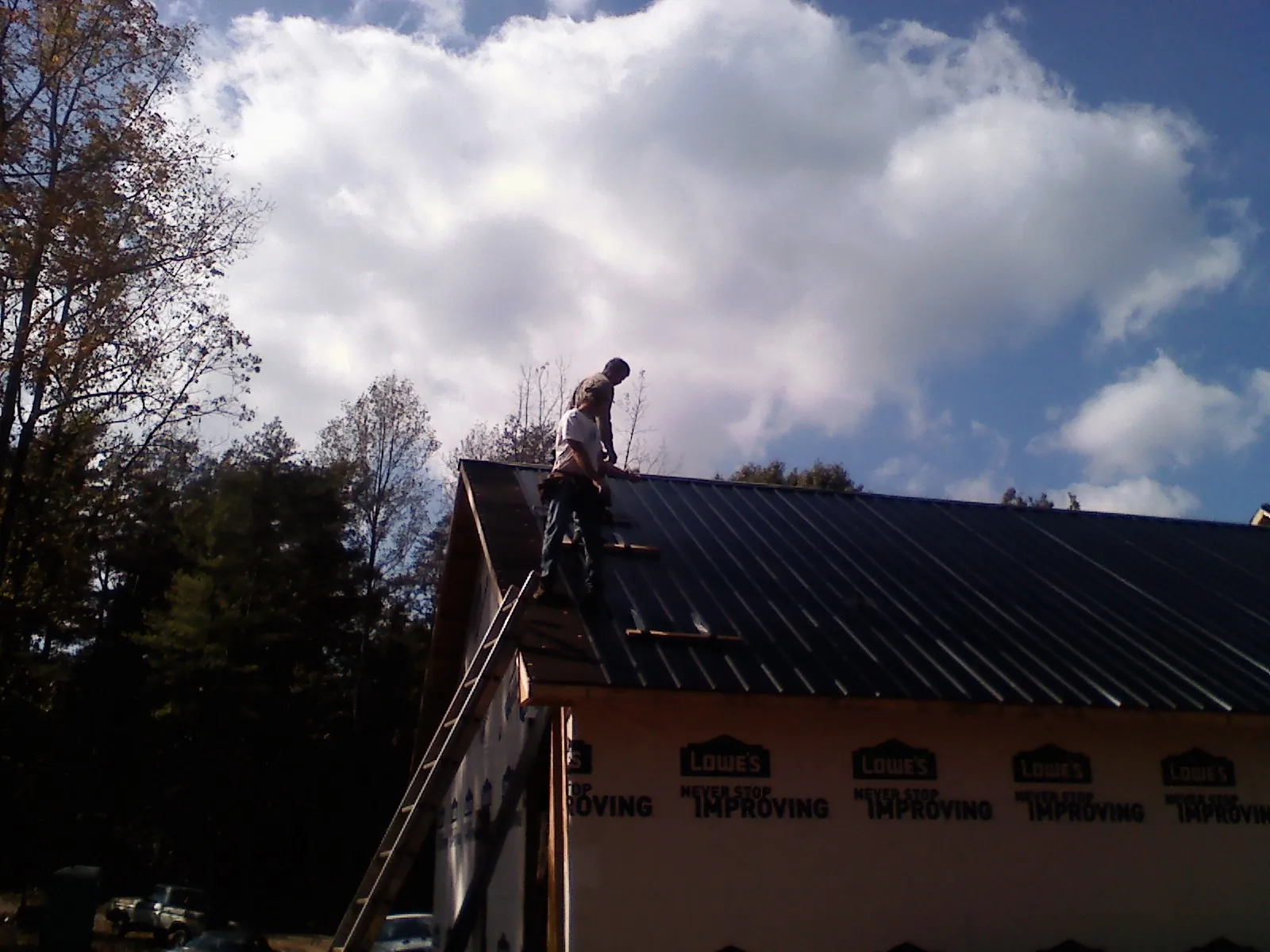 Roofer fastening dark metal panels high against a cloudy sky, from a Roof Inspection job in Mulberry