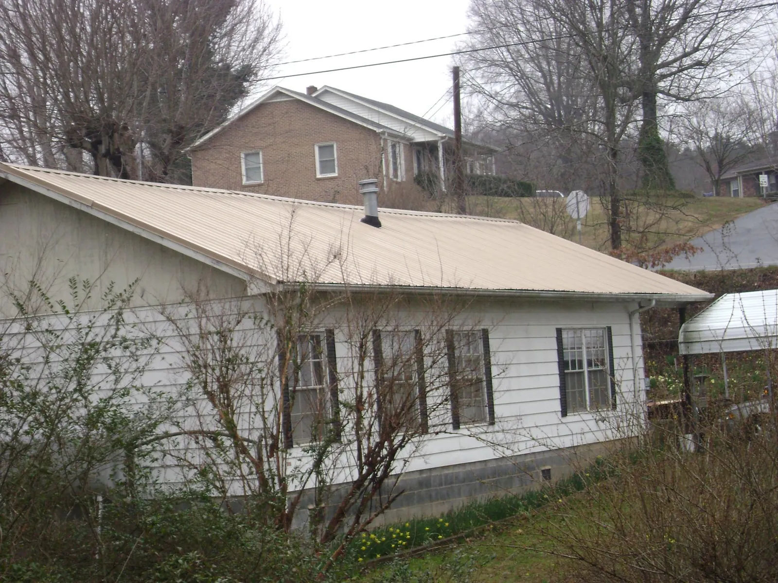 Tan metal roof on a white sided house set into a hillside — Commercial Roofing by Roofing Brothers in Mulberry